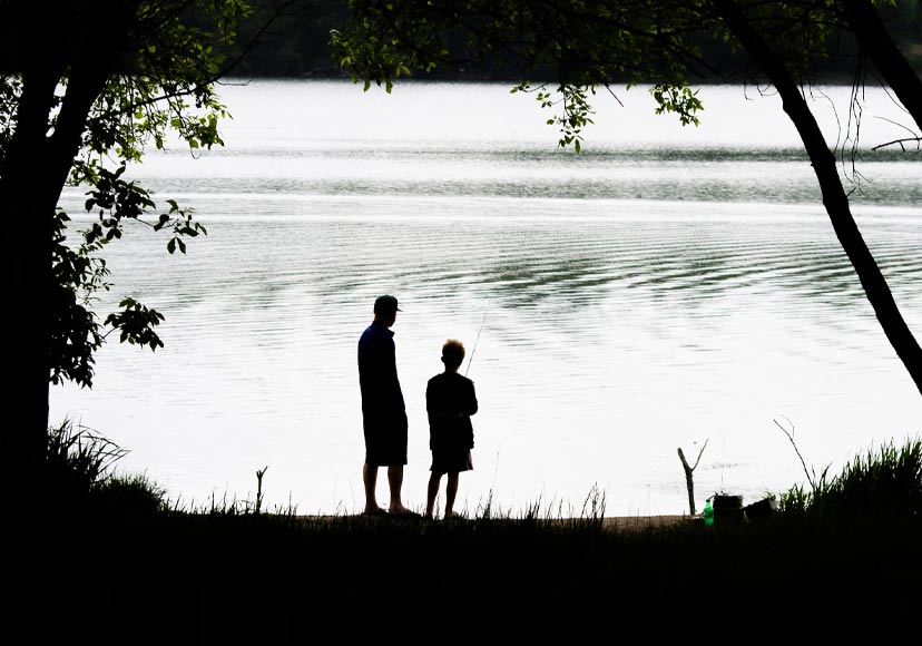 Father and son fishing by a lake.
