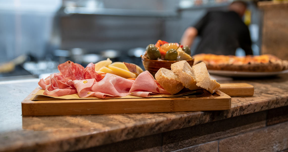 A pizza and breadboard of bread, olives and various italian hams freshly made at Il Colosseo.