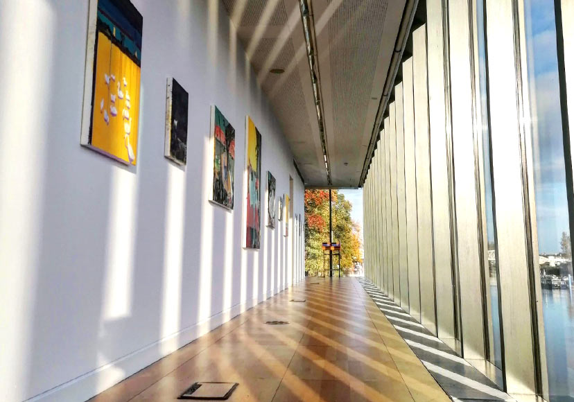 Paintings cast in sunlight along windowed hallway at the Luan Gallery.