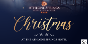 Elegant holiday setting inside Athlone Springs Hotel with two decorated Christmas trees by large windows, promoting a Christmas celebration at the hotel. Warm golden lights and festive ambiance.